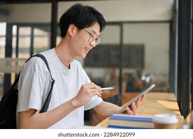Smart and handsome young Asian male college student using his digital tablet, working on school project, sitting in a coffee shop. - Powered by Shutterstock
