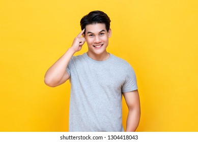 Smart Handsome Young Asian Man Thinking With Finger On Head Isolated On Colorful Yellow Background