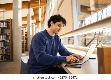 Smart Hispanic male student sitting at desk and using laptop, preparing diploma project in library campus. People. Education. Modern wireless technology. E-learning and distance communication concept - Powered by Shutterstock