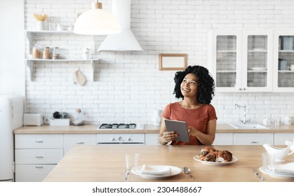 Smart Home Concept. Young black woman controlling house light with digital tablet, african american female using modern gadget to adjust lighting in kitchen, enjoying software for domestic comfort - Powered by Shutterstock