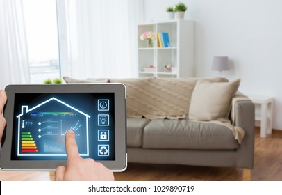 smart home and technology concept - close up of male hands pointing finger to tablet pc computer with house settings on screen over living room background