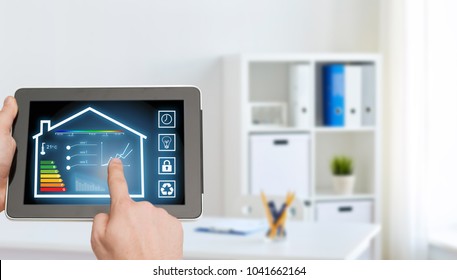 smart home and technology concept - close up of male hands pointing finger to tablet pc computer screen and regulating room temperature over office room background - Shutterstock ID 1041662164