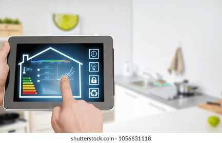 smart home and technology concept - close up of male hands pointing finger to tablet pc computer with house settings on screen over kitchen background - Shutterstock ID 1056631118