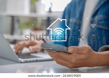Smart Home Technology with Wireless Network Control. Person using smartphone and laptop with Wi Fi and house icons, symbolizing IoT connectivity, remote access, and modern digital lifestyle at home.