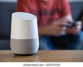 Smart Home Voice Activated Speaker In Lounge With Gamer In Background