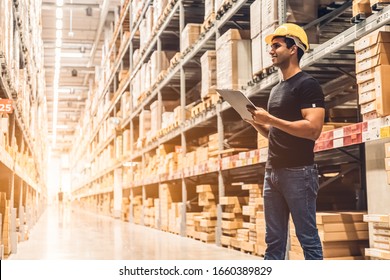 Smart Indian engineer man worker wearing safety helmet doing stocktaking of product management in cardboard box on shelves in warehouse. Factory physical inventory count.