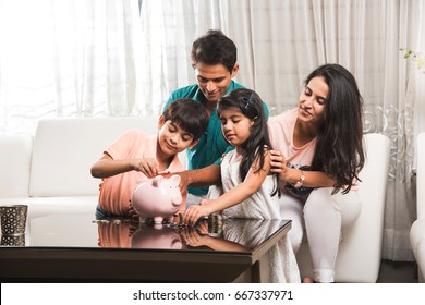 Smart Indian/asian Couple Teaching Importance Of Saving To Kids At Home With Piggy Bank