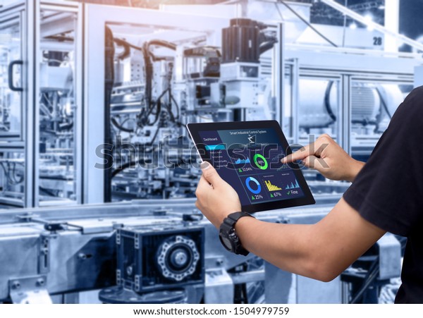 Smart industry control\
concept.Hands holding tablet on blurred automation machine as\
background