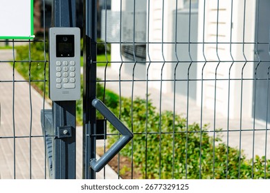 Smart intercom installed on a mesh fence. The device is equipped with a keyboard and a camera for video communication. It provides convenient access and security of the territory.