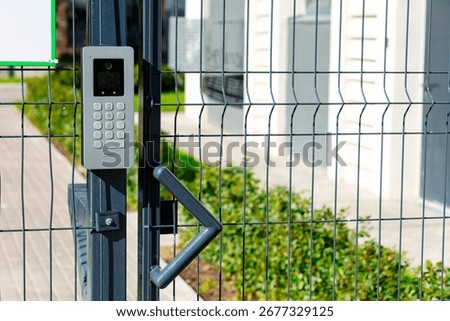 Smart intercom installed on a mesh fence. The device is equipped with a keyboard and a camera for video communication. It provides convenient access and security of the territory.