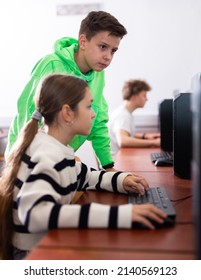 Smart interested preteen schoolboy helping cute girl classmate sitting at computer during informatics lesson..