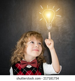 Smart Kid In Class. Happy Child Against Blackboard. Drawing Light Bulb. Idea Concept