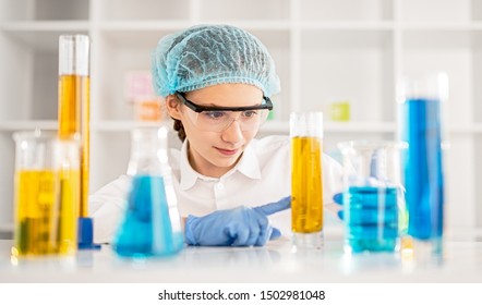 Smart Kid In Protective Clothes And Goggles Examining Flask With Chemical Fluid During Science Lesson At Modern School