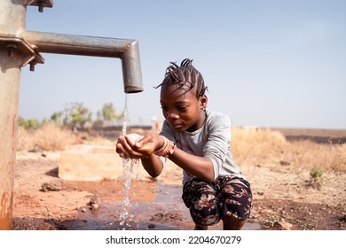 Smart little African girl kneeling in front of a tap collecting clean and fresh water; concept of lack of drinking water supply in rural areas - Powered by Shutterstock