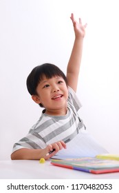 Smart Little Asian Boy Putting Up His Hand In Class To Answer A Question For His Teacher, Isolated On White Background