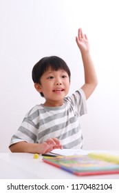 Smart Little Asian Boy Putting Up His Hand In Class To Answer A Question For His Teacher, Isolated On White Background