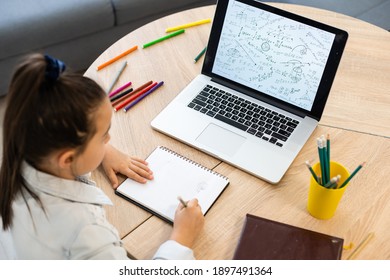 Smart Little Caucasian Girl Child Sit At Table Study At Laptop Make Notes Write In Notebook, Small Schoolgirl Handwrite Prepare Homework Assignment At Home, Distant Education Concept