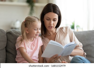 Smart Little Preschooler Girl Sit On Couch With Young Mother Or Nanny Reading Interesting Book At Home, Small Daughter Sturdy Learn With Mom At Home Enjoy Fairytale Spend Leisure Time Together