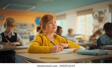 Smart Little Redhead Girl in Bright Clothes Sitting Behind a Desk in Primary School. Young Attentive Female Writing Down Notes in Notebook, Raising Hand in Order to Provide a Solution to an Exercise - Powered by Shutterstock