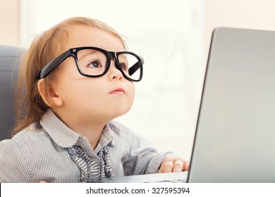Smart little toddler girl wearing big glasses while using her laptop