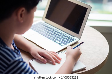 Smart Looking Asian Boy Studying Online Lesson With His Computer Laptop. Researching, Writing And Solving Problem With Concentration. Online Learning And Self Study Concept.