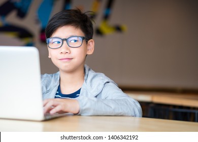 Smart looking Asian preteen boy with eye blue light blocking glasses rolling eyes smiling happily, using computer laptop to study online lessons. Online learning and self study concept. 