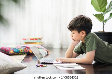 Smart Looking Asian Preteen Boy Lying On The Floor Using Notebook Computer In His Room He Putting Hands On Cheek And Looking At The Screen. Online Learning, Homeschool, New Normal, Home Based Learning