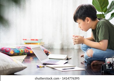 Smart Looking Asian Preteen Boy Use Laptop Computer At Home Study Lessons Through Online Learning And Teaching With Concentration Due To Covid-19 Pandemic And Social Distancing Measures