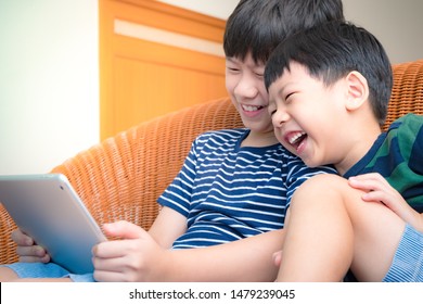 Smart Looking Asian Preteen Boy And His Adorable Little Brother Laughing Together, Watch Funny Cartoon On Tablet With Joy. Happy Brotherhood Moment, Children With Digital Entertainment, Gamification.