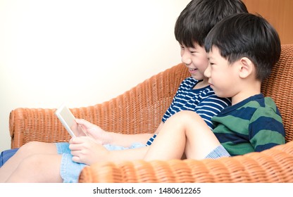 Smart Looking Asian Preteen Boy And His Adorable Little Brother Joyful Watching Funny Cartoon On Tablet Together. Happy Brotherhood Moment, Children With Digital Entertainment, Gamification, Kids Tech