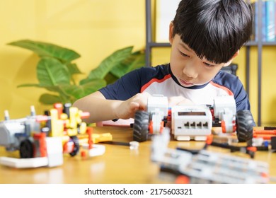 Smart looking Asian student kid assembling robot, coding and solving engineering problem at home with yellow wall in background. STEM education and 21st century learning skills concept - Shutterstock ID 2175603321