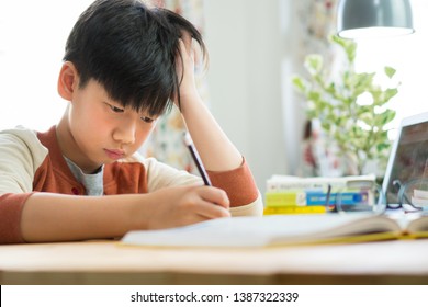 Smart Looking Asian Teen Boy Is Studying Hard And Writing Homework With Concentration, Feeling Tired, Drained, Stressed, Frustrated And Overwhelmed. One Hand Pulls His Messy Hair. Teenage, Preteen.