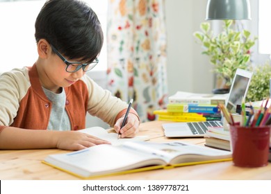 Smart Looking Asian Teen Boy Wear Glasses, Write Homework, Take Notes From Online Lessons, Preparing For The Exam Due To Pandemic Of Covid-19 And Social Distancing. Online Learning Technology. Preteen