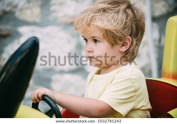 Smart\
looking boy. Kid playing car with very serious clever look. Curly\
blond hair boy. Modern children. Small driver. Driving school,\
child driving, amusement park for\
children\
