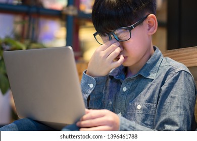 Smart Looking Tween / Preteen Asian Boy Wears Blue Light Blocking Glasses From LED Computer, Squeezes His Nose As His Eyes Strained, Stressed From Long Screen Exposure.  Computer Vision Syndrome (CVS)