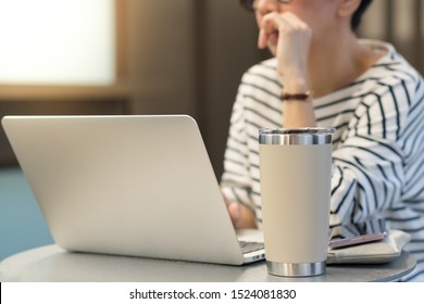 Smart looking woman use laptop computer to work from home due to Covid-19 pandemic, city lockdown and social distancing with her drink in a reusable stainless steel tumbler mug aside. - Powered by Shutterstock