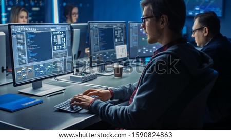 Smart Male IT Programer Working on Desktop Green Mock-up Screen Computer in Data Center System Control Room. Team of Young Professionals Programming Sophisticated Code