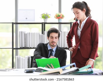 Smart Man And Woman In Suits Examining And Discussing Papers With Serious Face Against Shelf And Window While Working In Modern Workplace Together