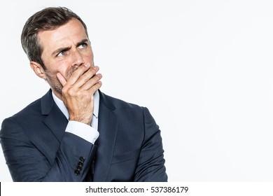 smart middle aged businessman thinking, looking up with hand hiding his mouth, expressing leadership reflections and concerns, copy space, white background studio - Powered by Shutterstock