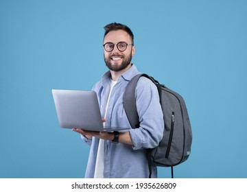 Smart Millennial Student With Backpack Using Laptop Computer Over Blue Studio Background