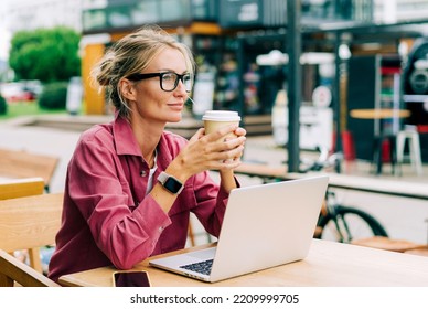 Smart modern woman sitting in a coffee shop drinking coffee and working on a laptop remotely. - Powered by Shutterstock