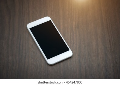 Smart phone with blank screen lying on wooden table- sunlight filter effect