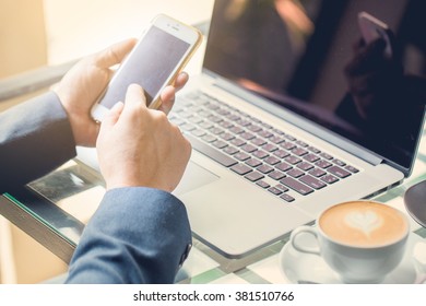 Smart phone in businessman hand with laptop and coffee