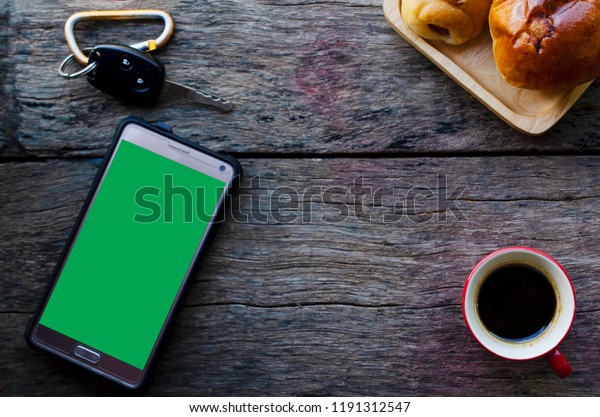 Smart phone and Car key with green\
screen and red coffee cup on wood backgrounds\
above
