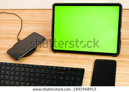 Smart phone is charging on wireless charging next to the tablet with chromo key and keyboard.