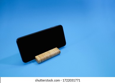 A Smart Phone Desk Holder In Wooden Block Isolated On Blue Background.  Technology And Lifestyle Concept 