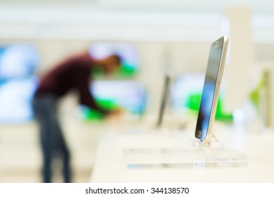 Smart Phone In Focus At Mobile Store. Man Is Out Of Focus In Background Looking For Some New Smart Phone For Him. Shallow Depth Of Field.