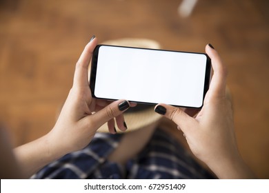 Graue Farbe für Smartphone. Junge Frauen mit schwarzem Nagellack, die mit dem Handy auf rustikalem braunem Holzhintergrund spielen. Unscharfer weißer Bildschirm.