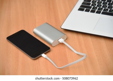 Smart Phone And Laptop With Charger Power Bank On Wood Table. Power Bank Charging Smart Phone.