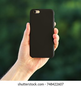 Smart Phone On The Blurred Background Of The Park In A Black Plastic Case Back View. Smart Phone In Man's Hand. Template Of Phone Case